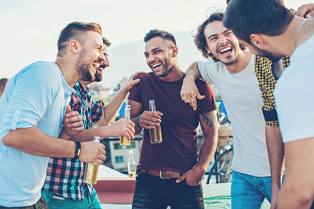 Multi-ethnic group of young men chatting and drinking beer on a rooftop party.